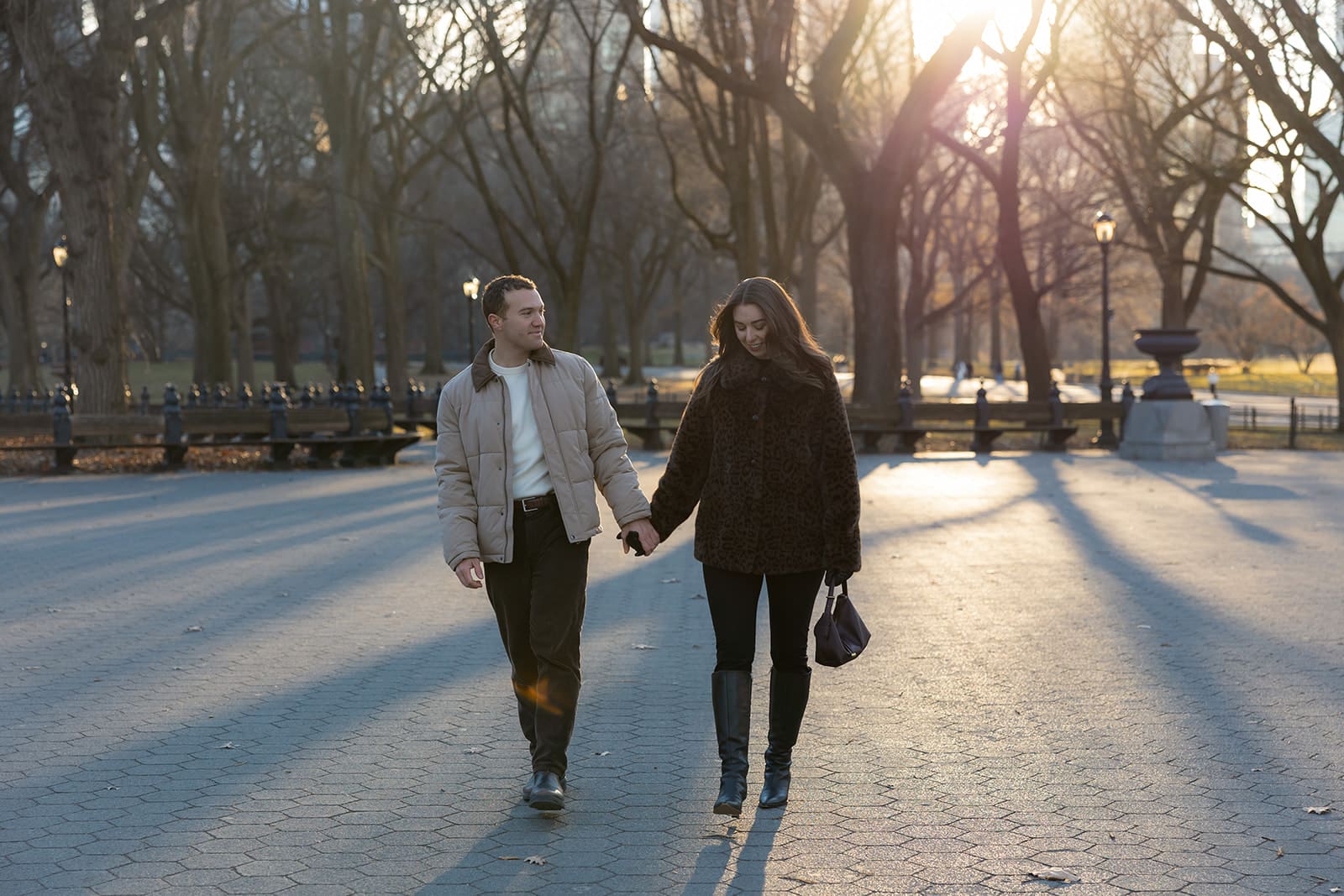 Carlie and Mat walking hand in hand through Central Park in the late winter light