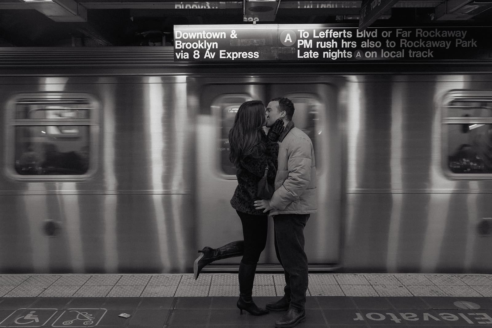 Carlie and Mat kissing as a New York City subway train passes behind them
