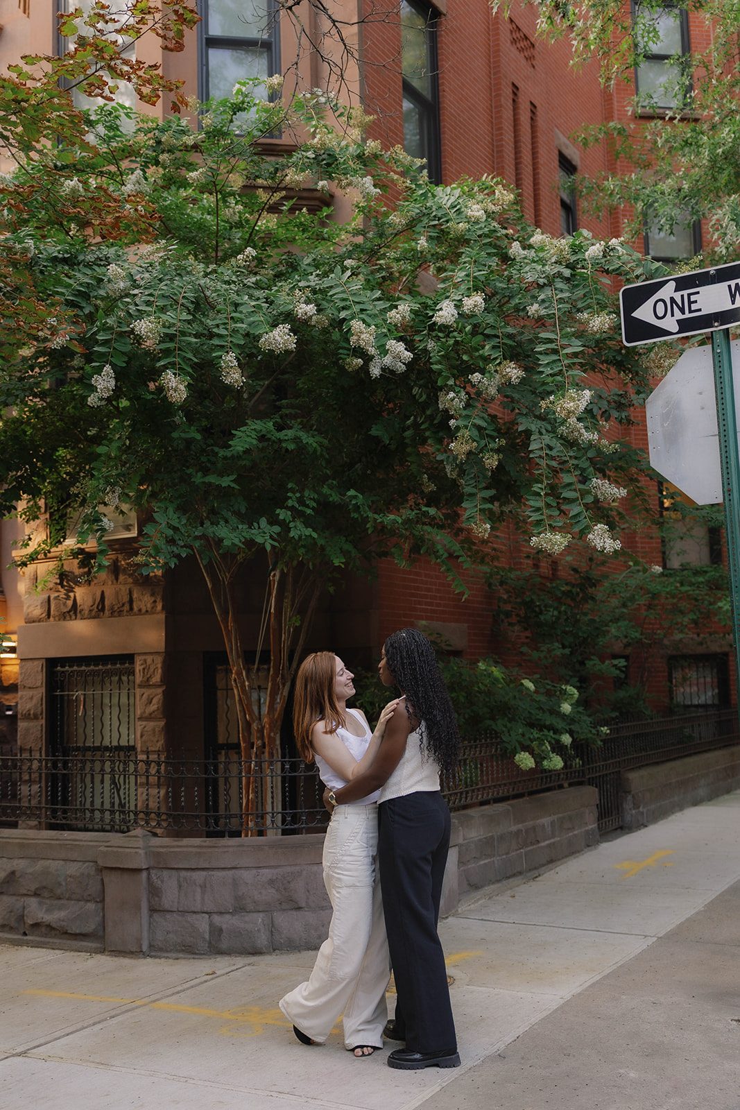 Cassia and Laura standing together beneath flowering trees on a Park Slope brownstone street