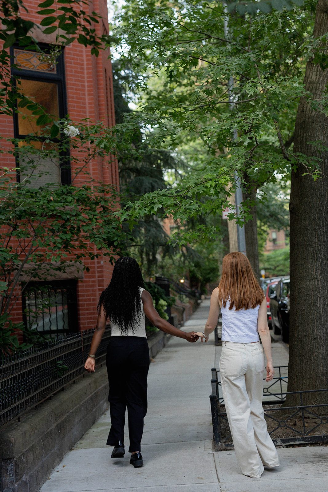 Cassia and Laura walking hand in hand down a tree-lined Park Slope street