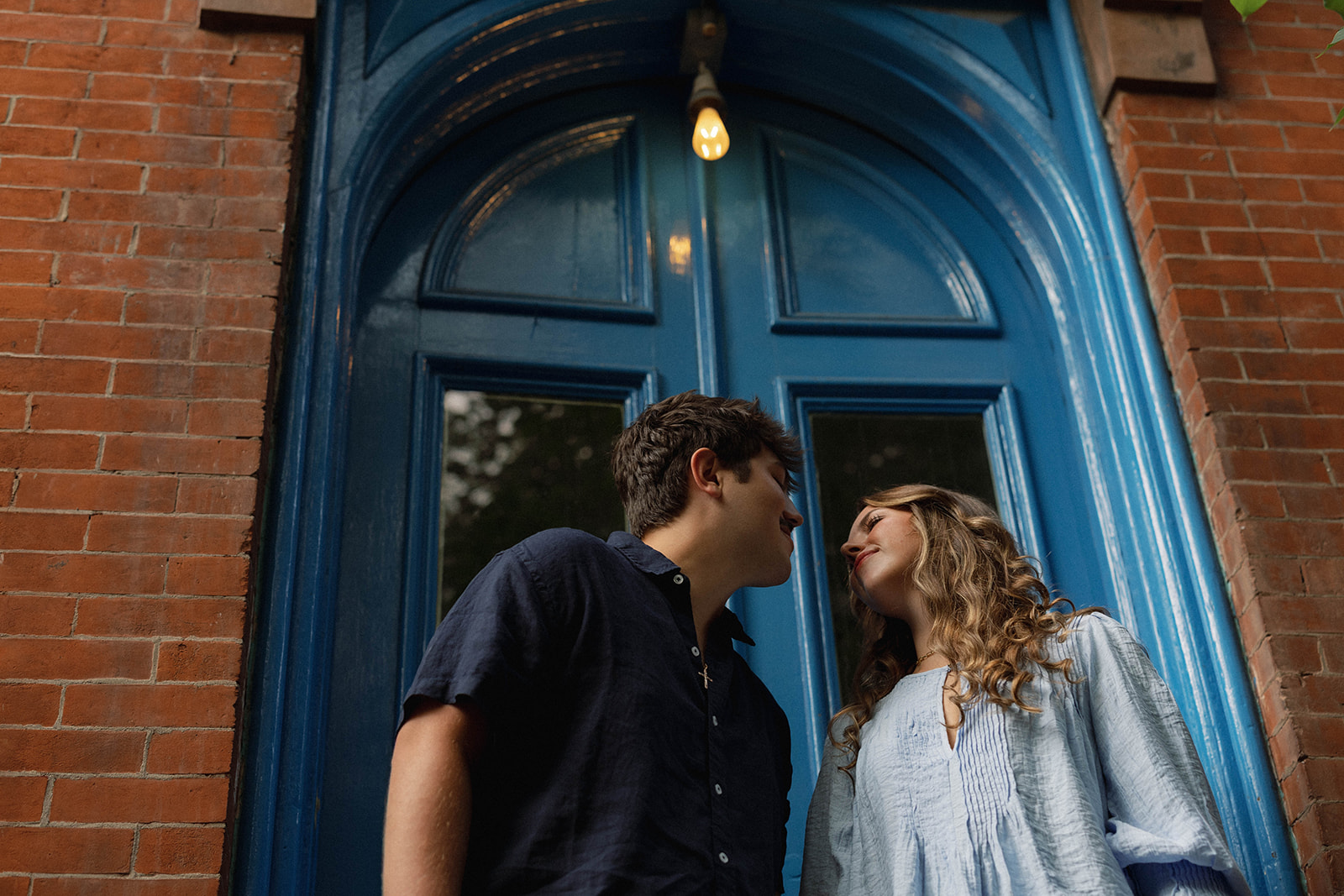 Sadie and David leaning toward each other beneath a blue Brooklyn doorway