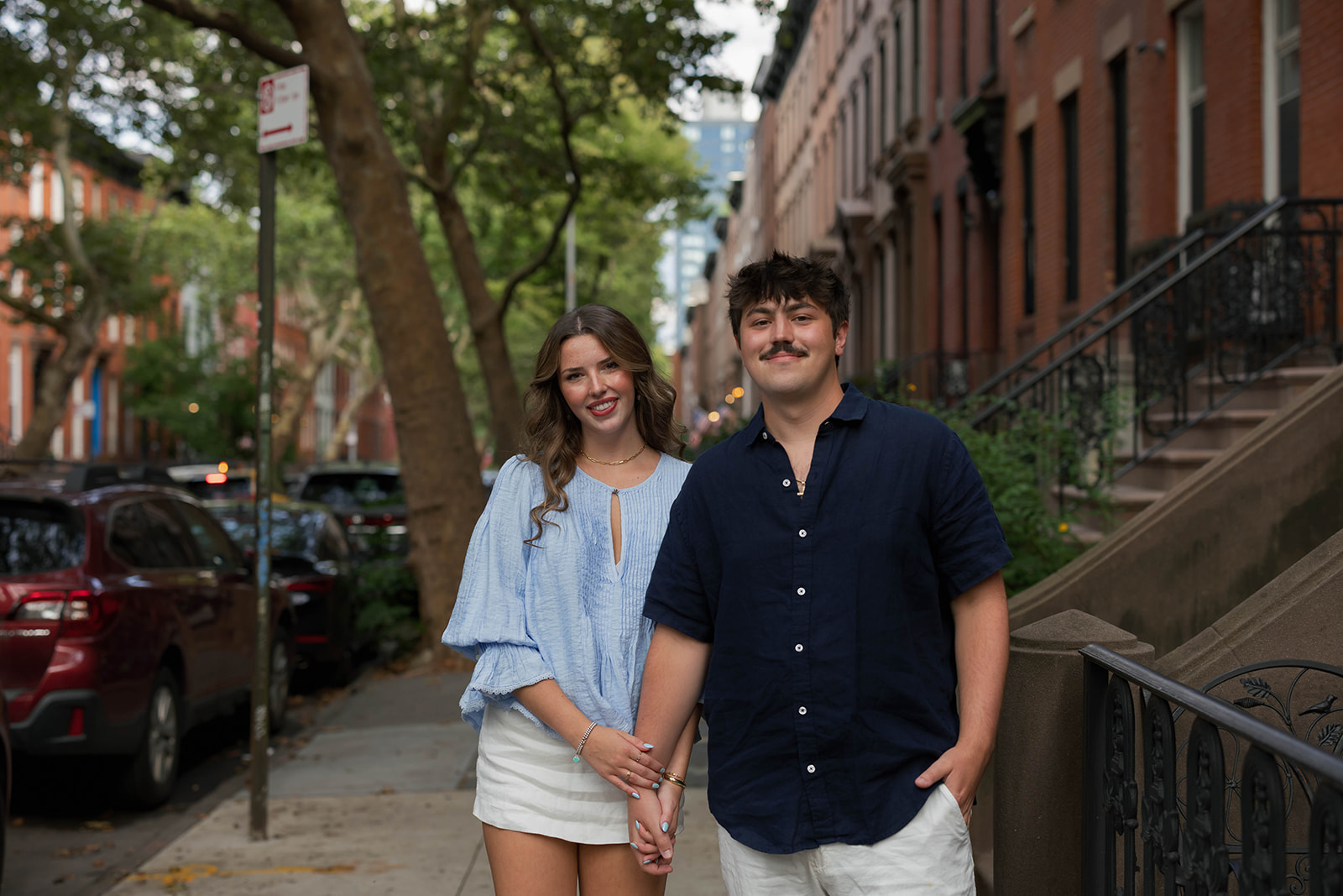 Sadie and David holding hands on a tree-lined Brooklyn brownstone block