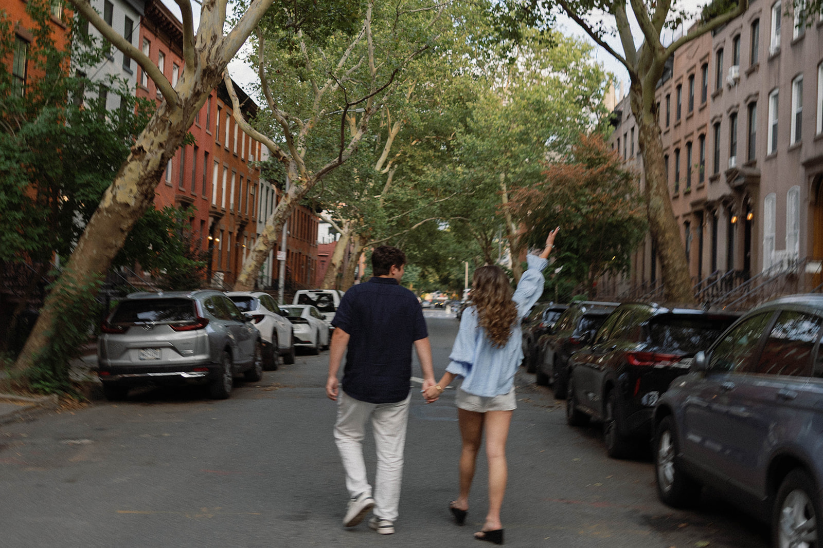 Sadie and David walking hand in hand down a tree-lined Brooklyn street