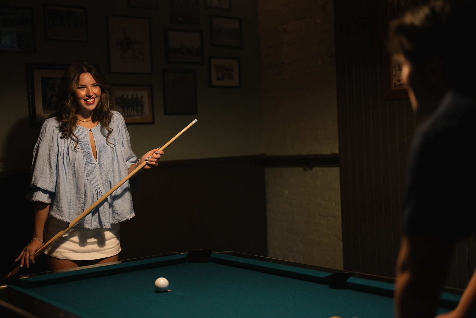 Sadie smiling across the pool table in warm window light at Brooklyn Social